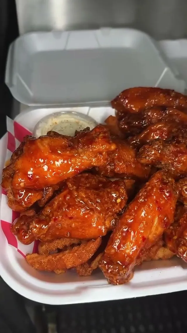 Glossy buffalo wings piled in a takeout tray